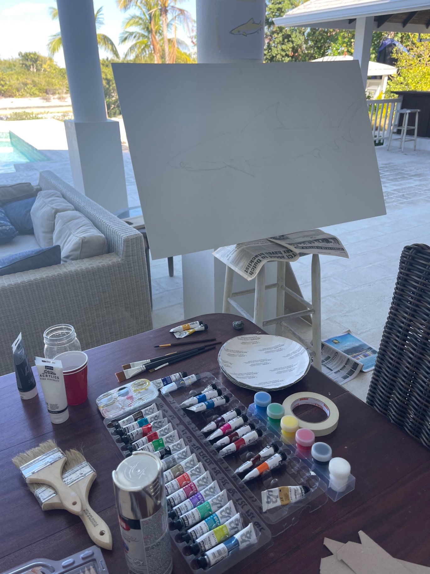 Outdoor studio table with paints, brushes and a drawn-out canvas on an easel