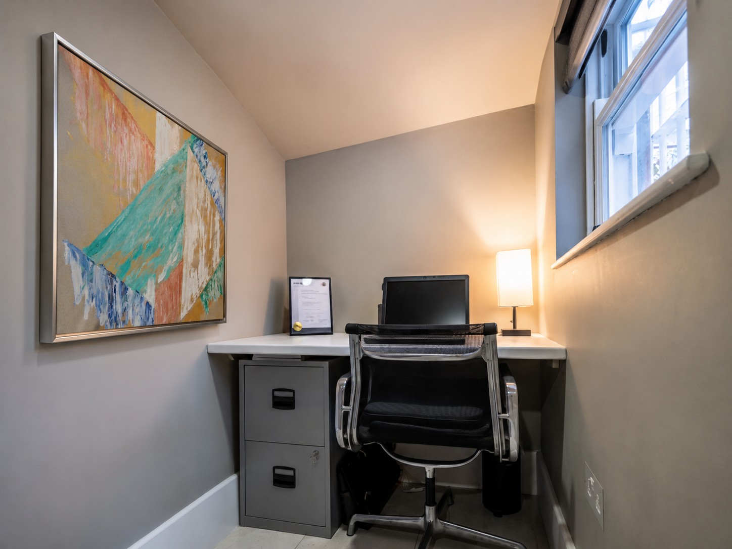 A pale geometric painting above a small desk
